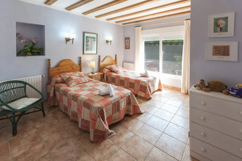 Un dormitorio luminoso con dos camas y una ventana grande con vistas a la vegetación.