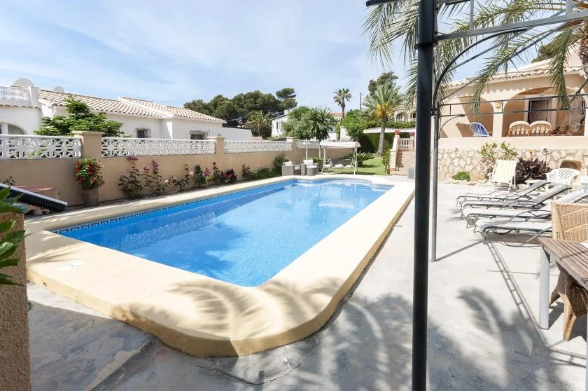Una piscina exterior soleada está rodeada de tumbonas y asientos de patio.