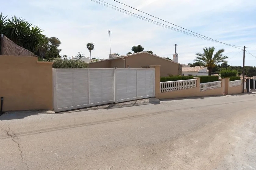 Una casa beige está detrás de una puerta metálica clara junto a una calle residencial.