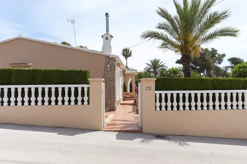 La entrada de un edificio amurallado da a un camino pavimentado, con una palmera detrás.