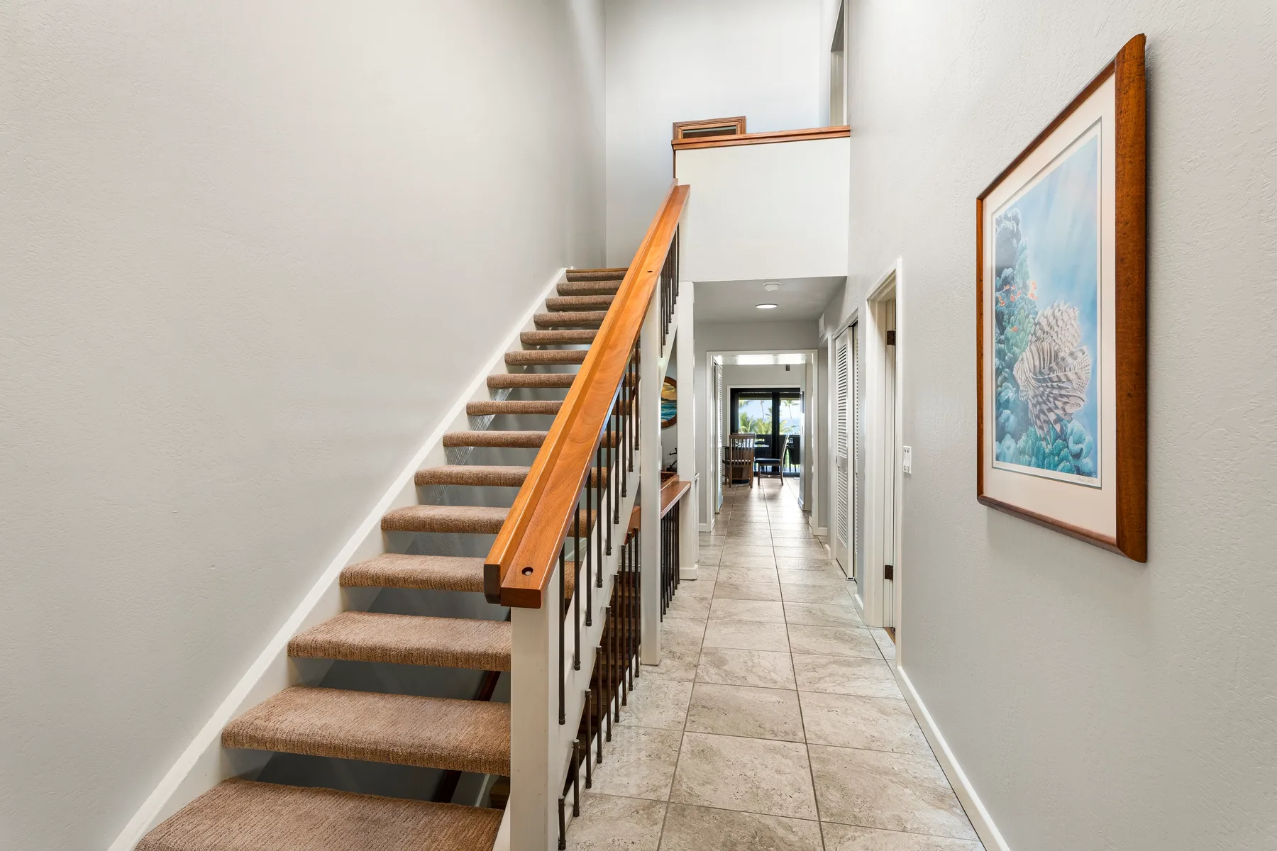 Un pasillo interior con una escalera y una obra enmarcada en la pared.
