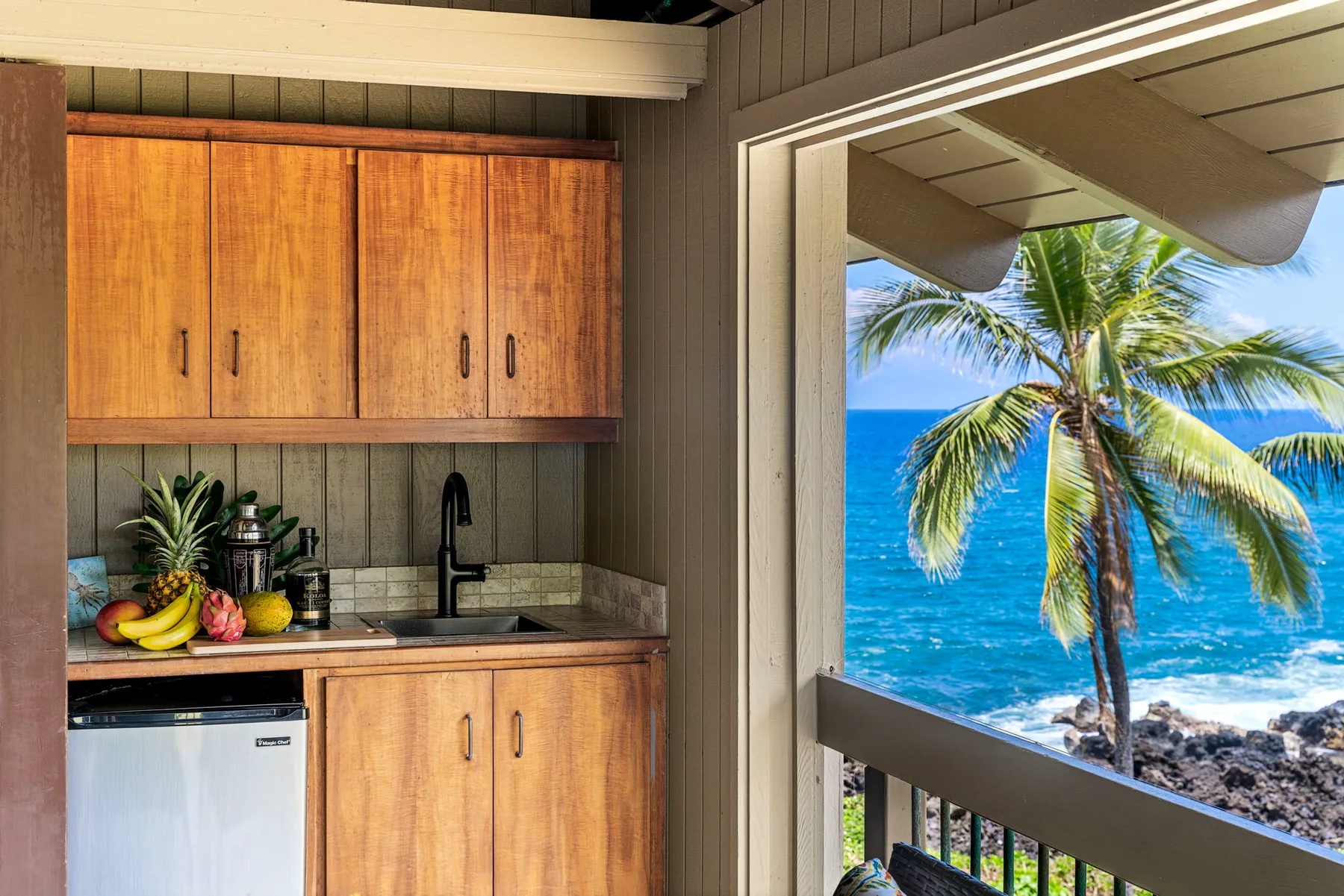 Una cocina compacta da a un balcón con una palmera y vistas al mar.
