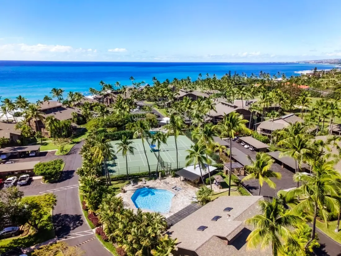 Vista aérea de un complejo tropical con piscina, canchas de tenis y el océano al fondo.