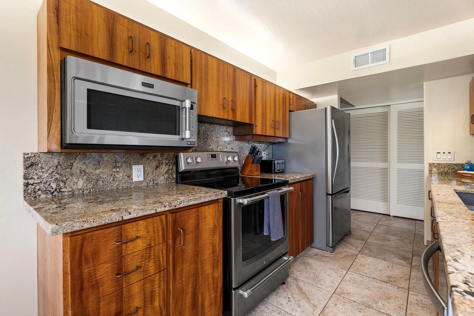 Una cocina con gabinetes de madera, un refrigerador y electrodomésticos para cocinar.