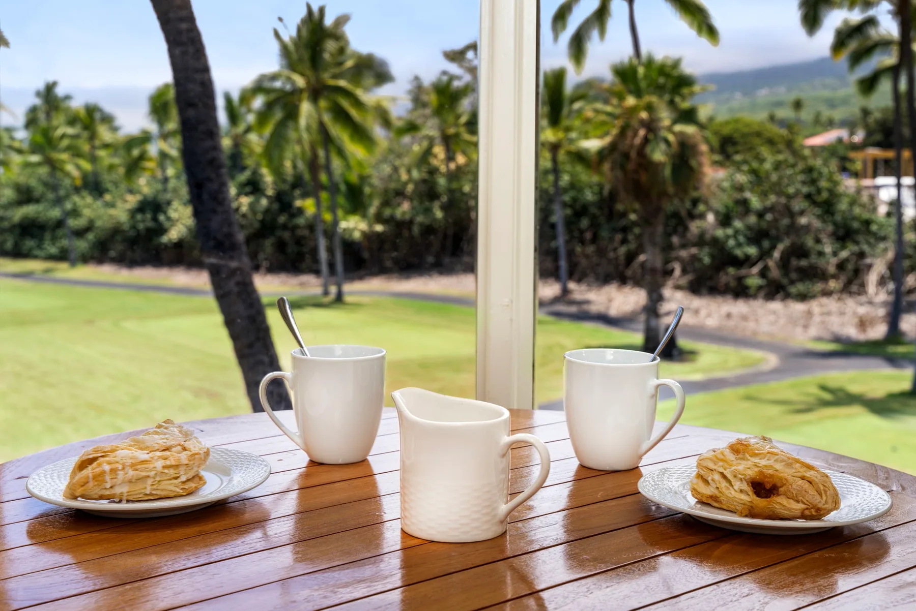 Una mesa con tazas y pasteles da a un jardín verde a través de una ventana.