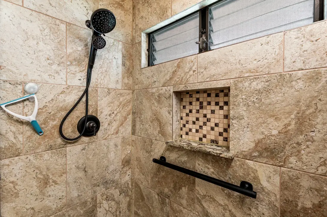 Una zona de ducha revestida de azulejos, con una ducha de mano y un nicho.