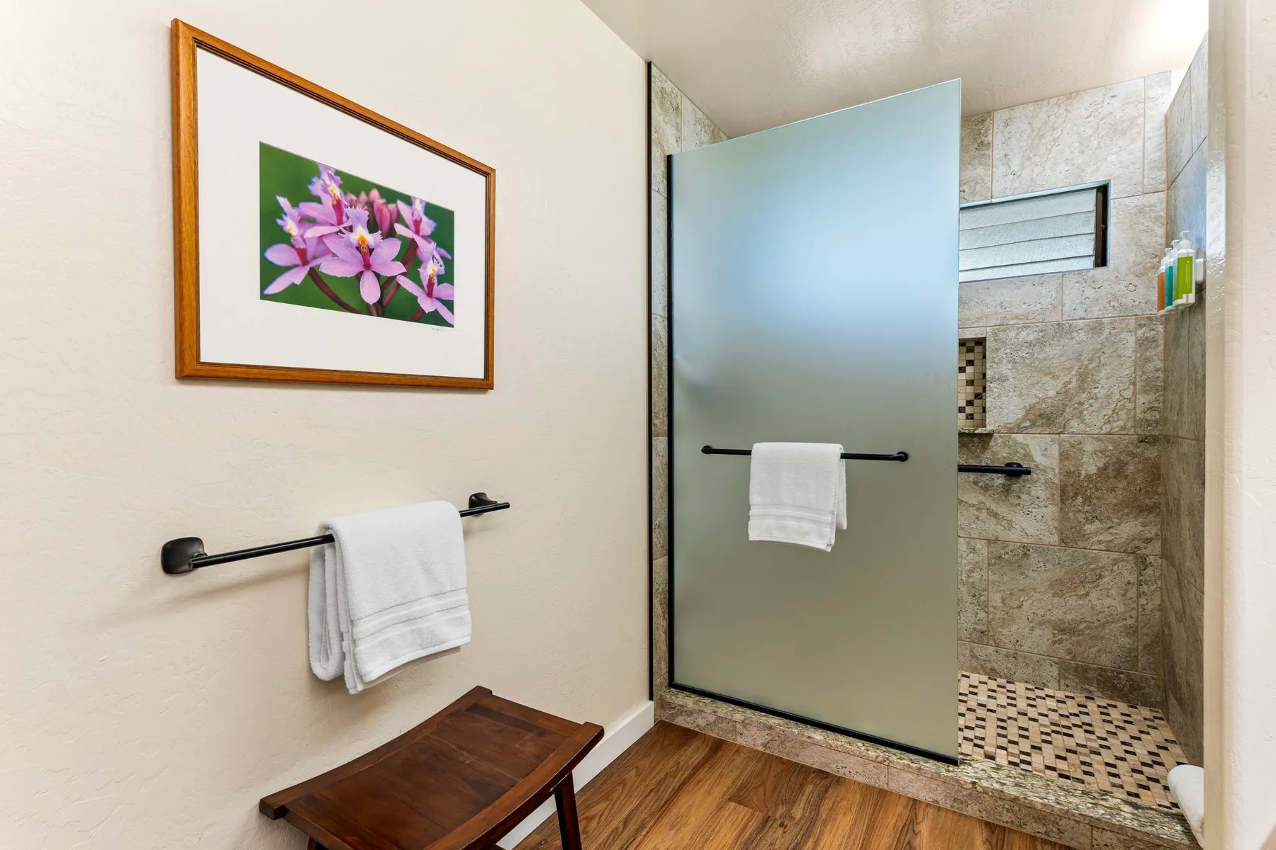 Un baño con ducha de vidrio, barras para toallas y un cuadro floral enmarcado.