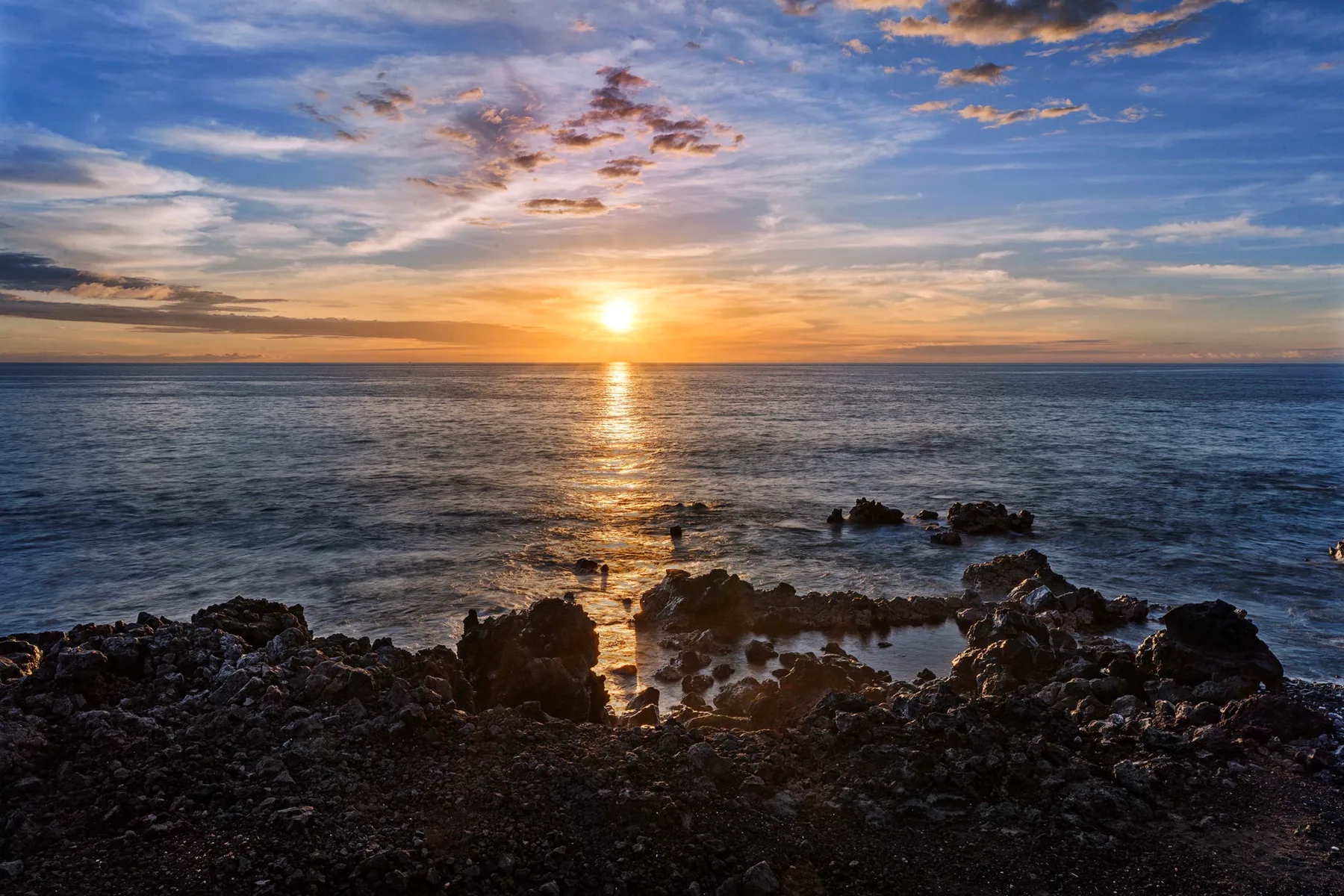 Un atardecer sobre el océano, con olas que bañan una costa rocosa.