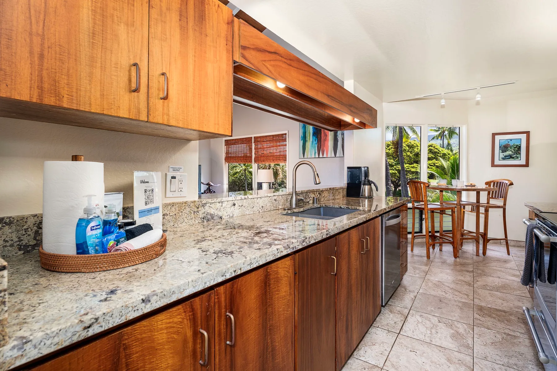Una cocina con gabinetes de madera, una encimera larga y una mesa de comedor junto a las ventanas.