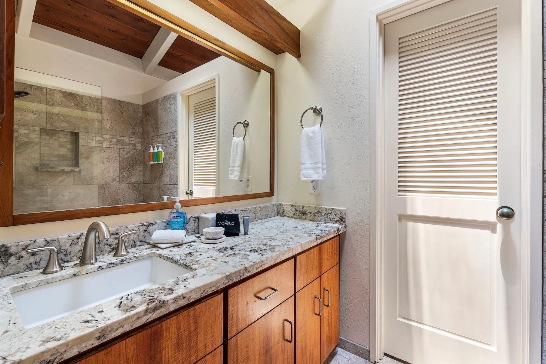 Un lavabo de baño con un espejo amplio, una encimera de piedra y armarios de madera.