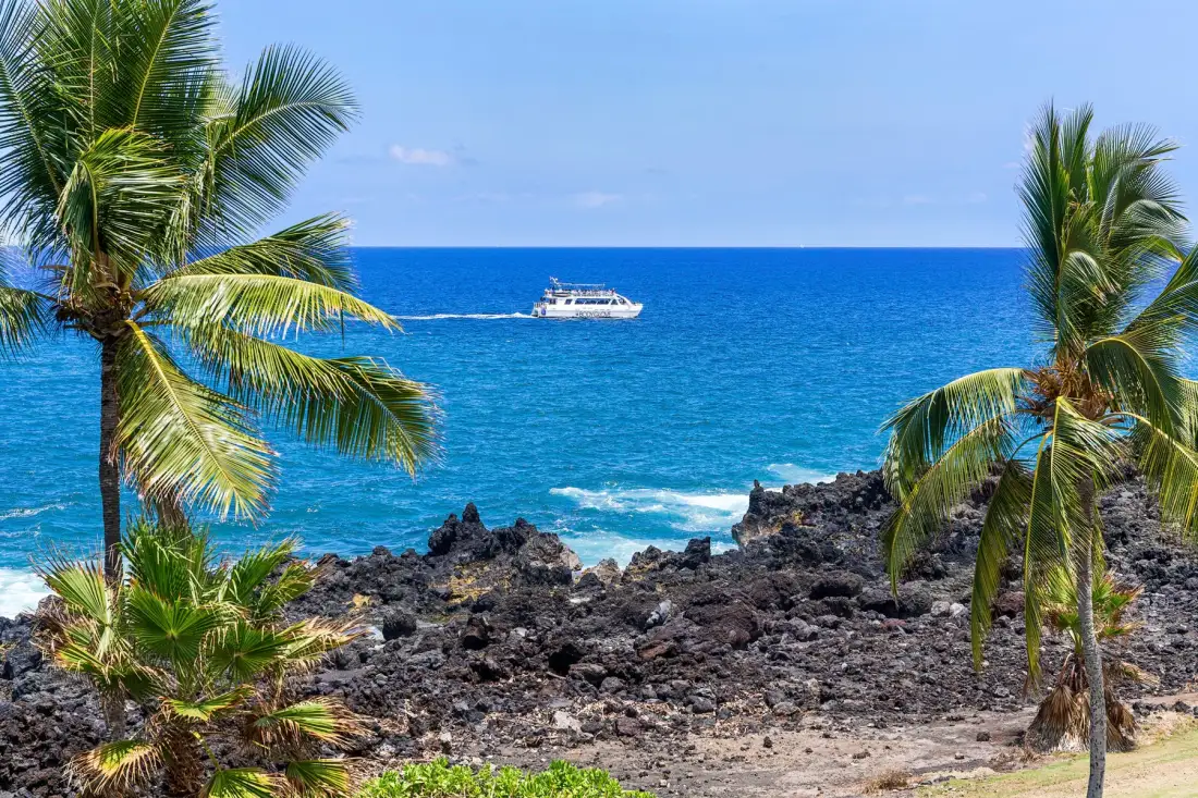 Una costa tropical rocosa con palmeras y un barco en el mar azul.