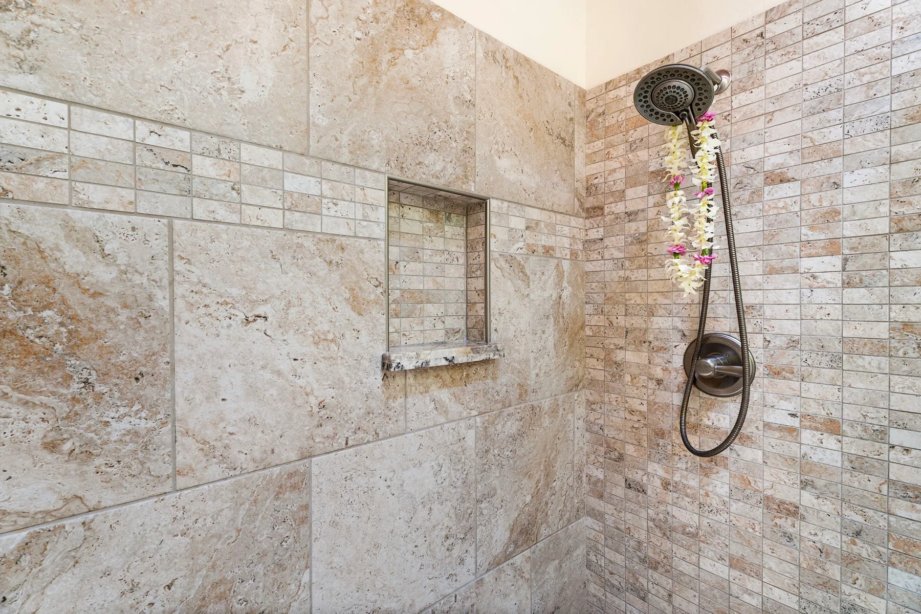 Una ducha con azulejos, un nicho empotrado en la pared y una ducha de mano.