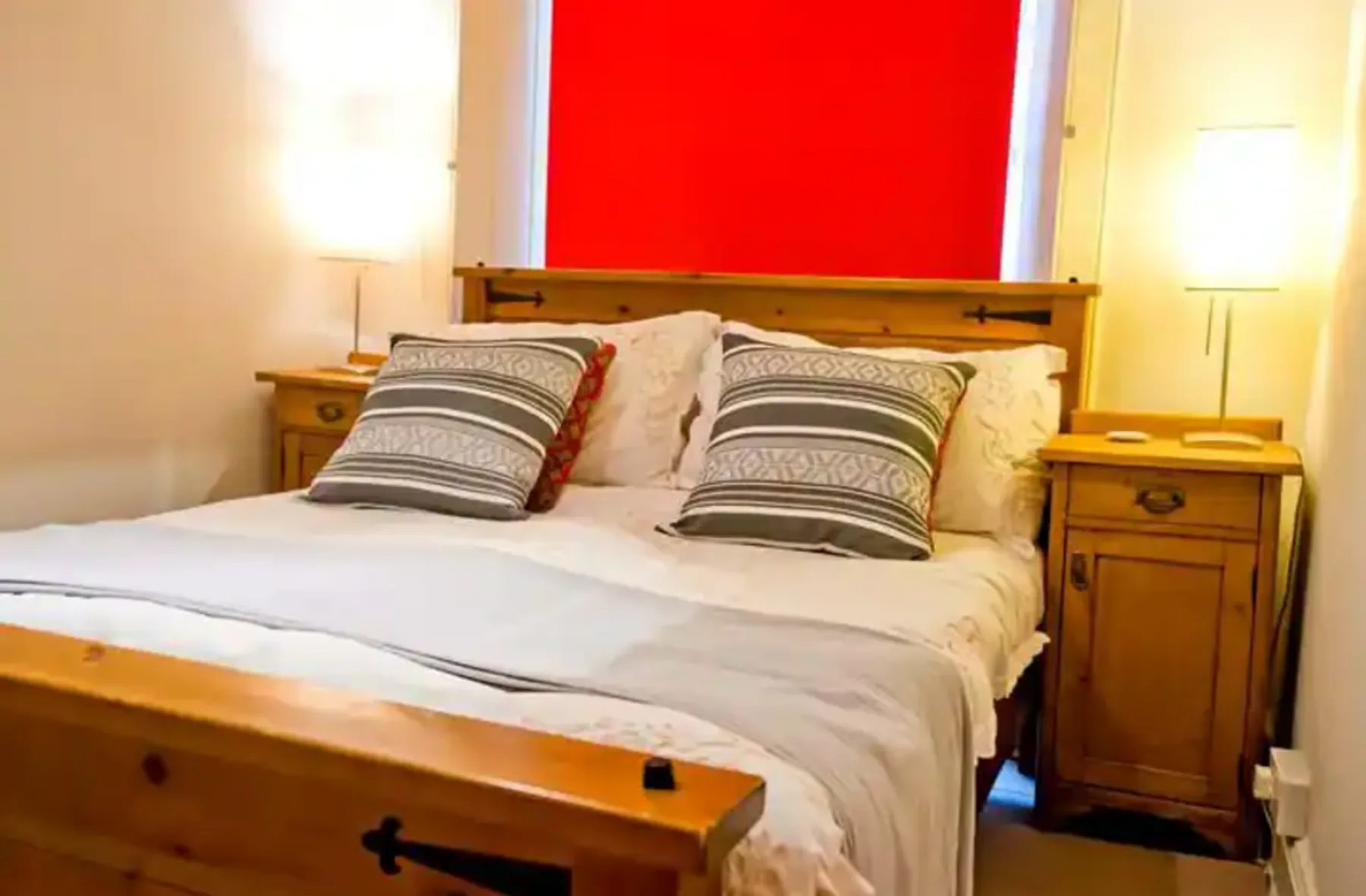 A bedroom with a wooden bed and bedside tables beneath a bright red wall panel.