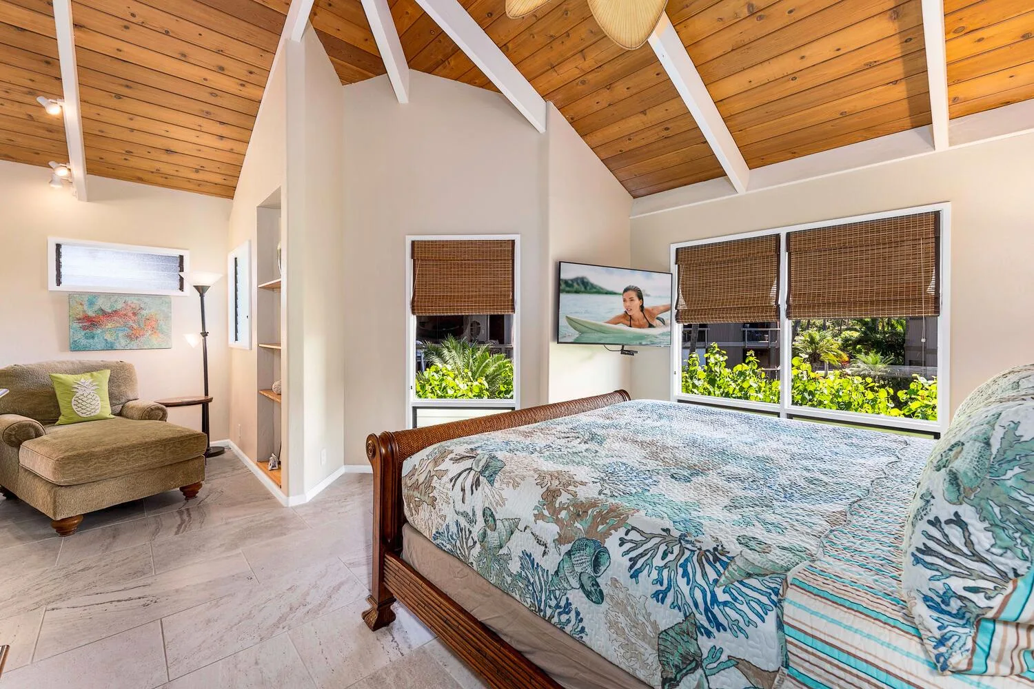 Un dormitorio con una cama grande, una zona de estar y ventanas bajo un techo abovedado de madera.
