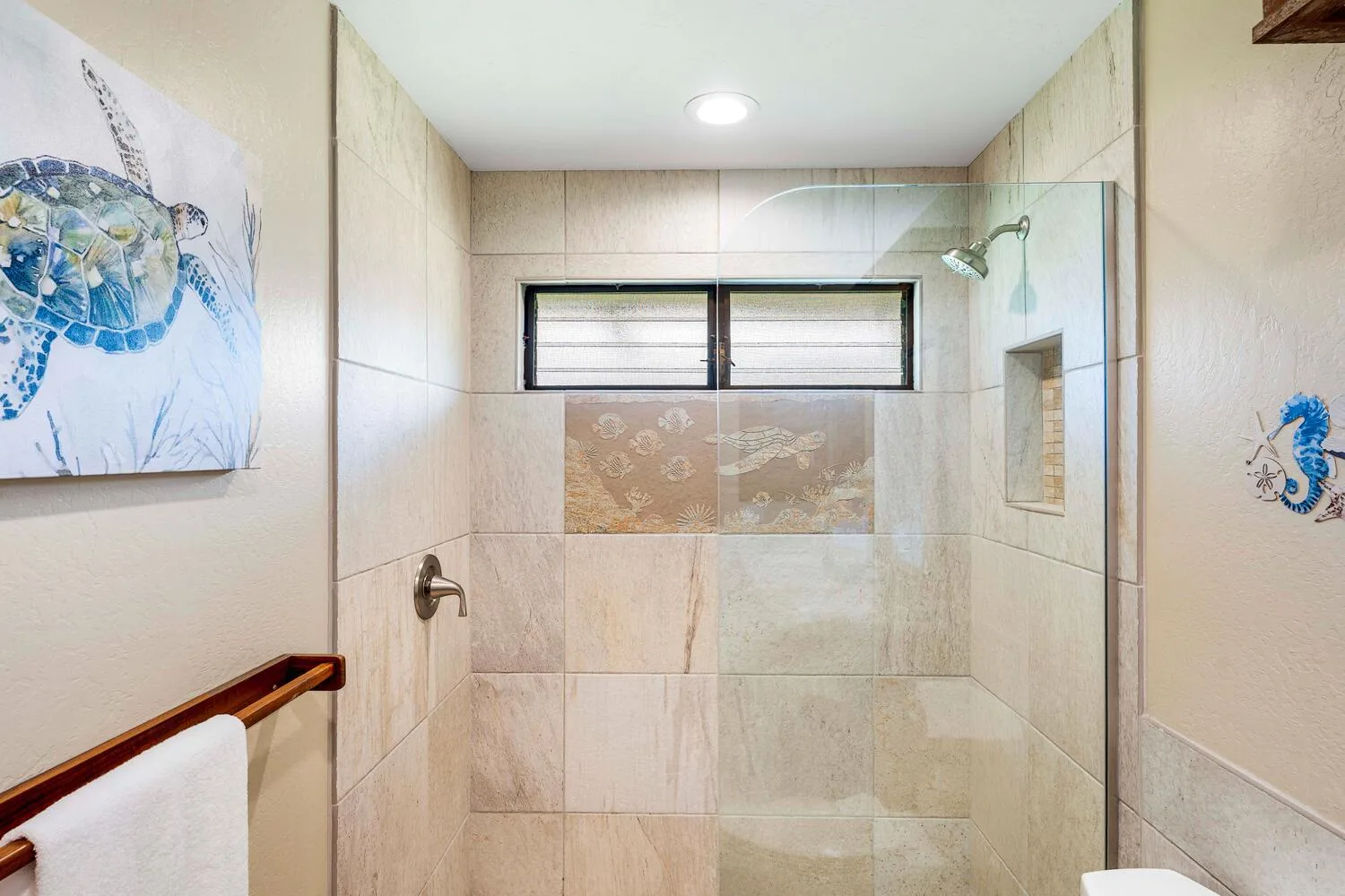 Un baño revestido de azulejos con ducha de vidrio y una ventana alta pequeña.