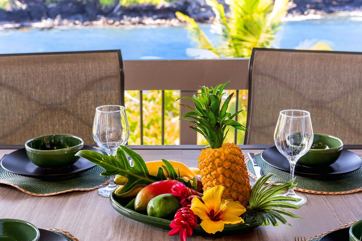 Una mesa está preparada con fruta tropical y vajilla junto a una barandilla de balcón.