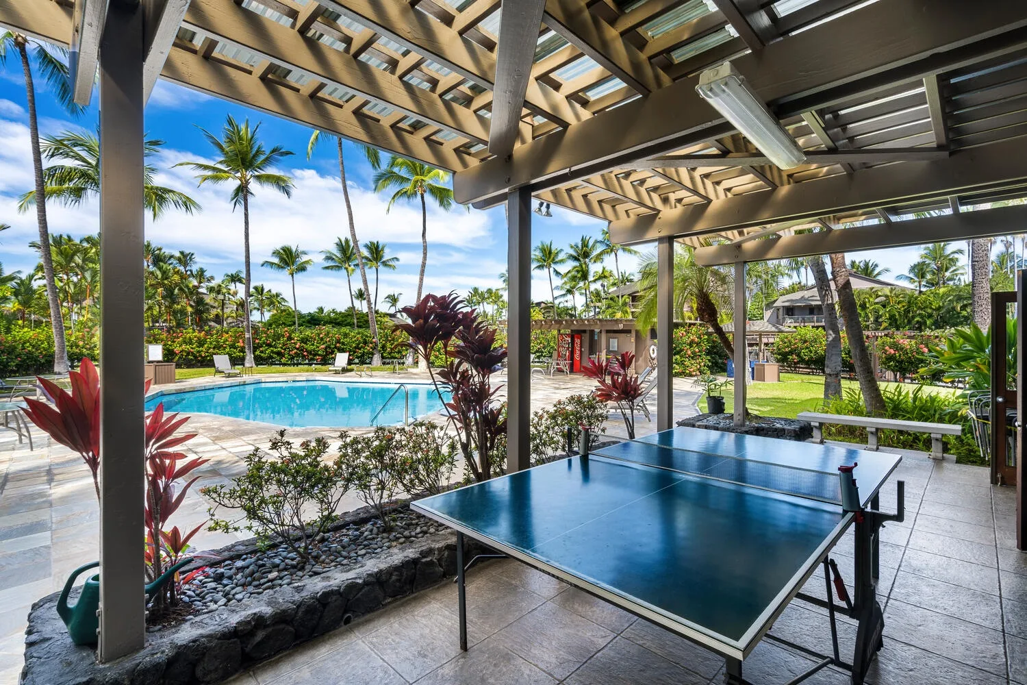 Un patio cubierto con una mesa de ping-pong da a una piscina y un jardín tropical.