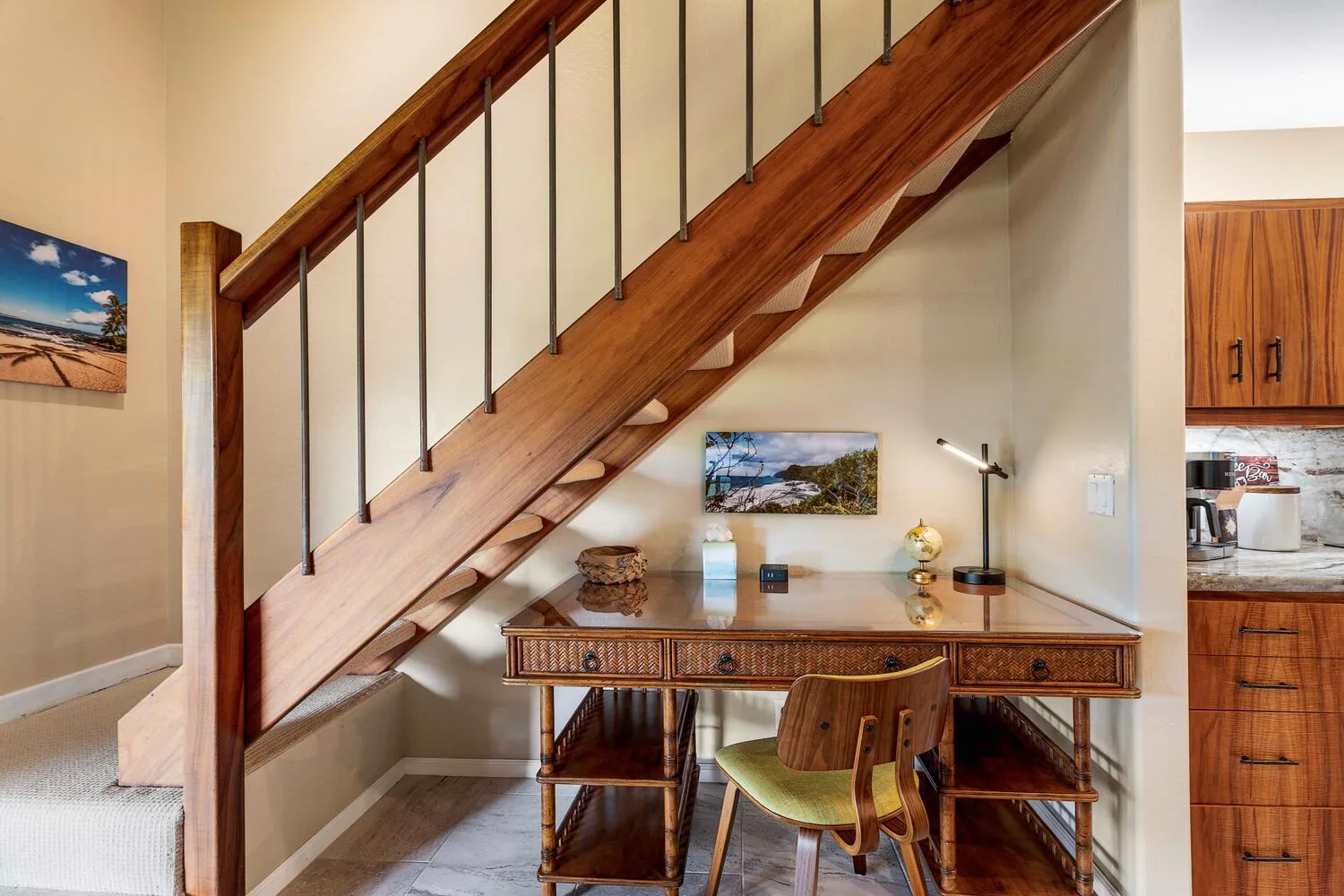 Un escritorio y asientos están bajo una escalera de madera en un interior luminoso.