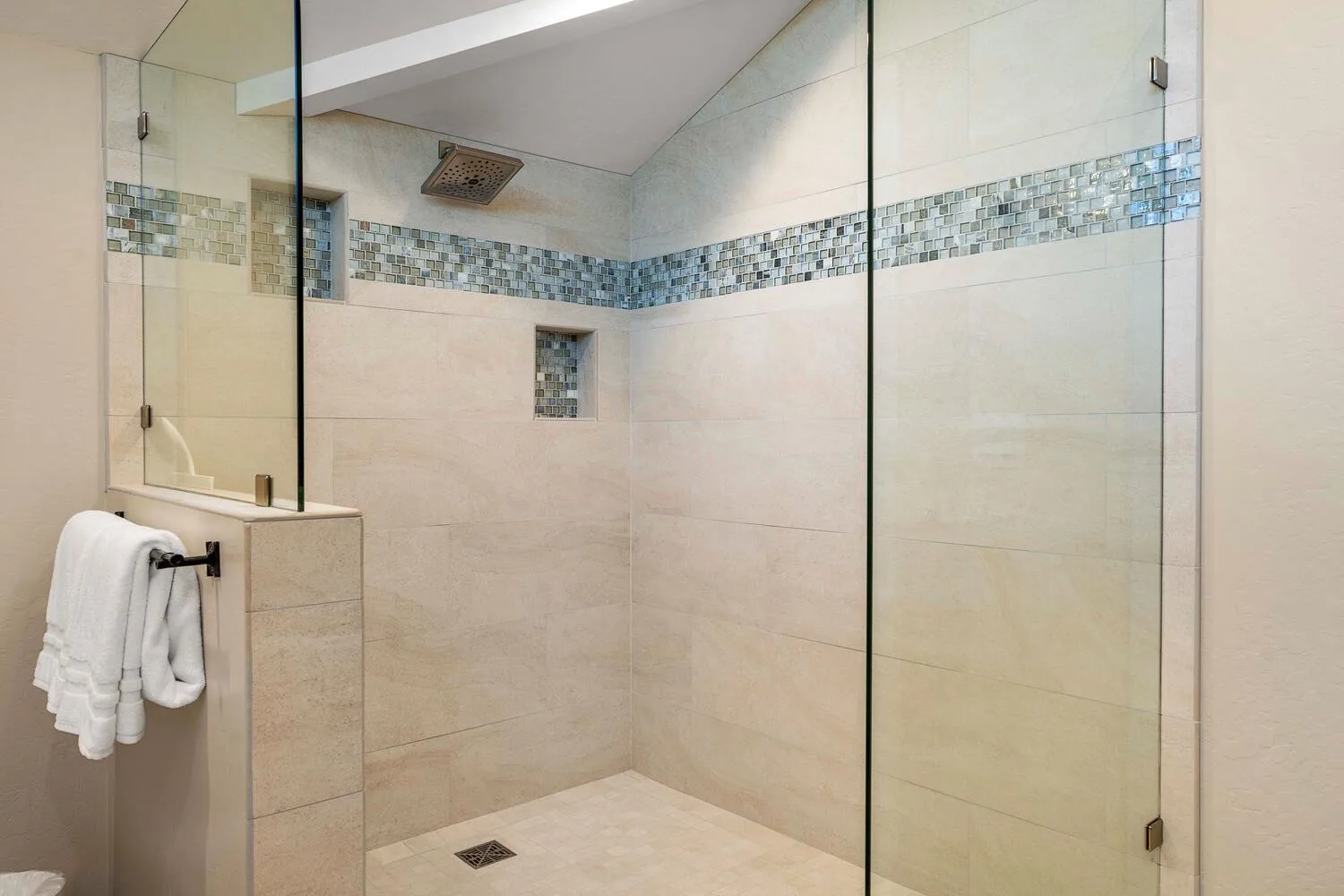 Una ducha revestida de azulejos, con paneles de vidrio y una franja decorativa de mosaicos azules.