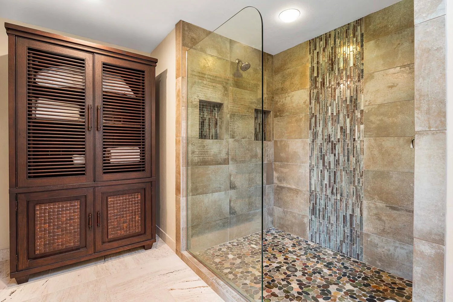 Zona de ducha con azulejos, mampara de vidrio y armario de madera oscura.