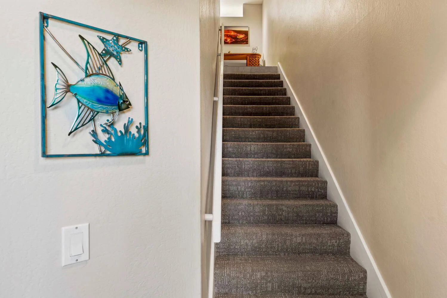Una escalera interior con peldaños alfombrados y arte de peces en la pared.