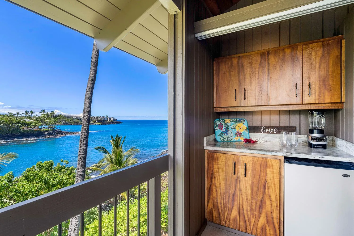 Una pequeña cocina con gabinetes de madera da a un balcón con vista al mar.