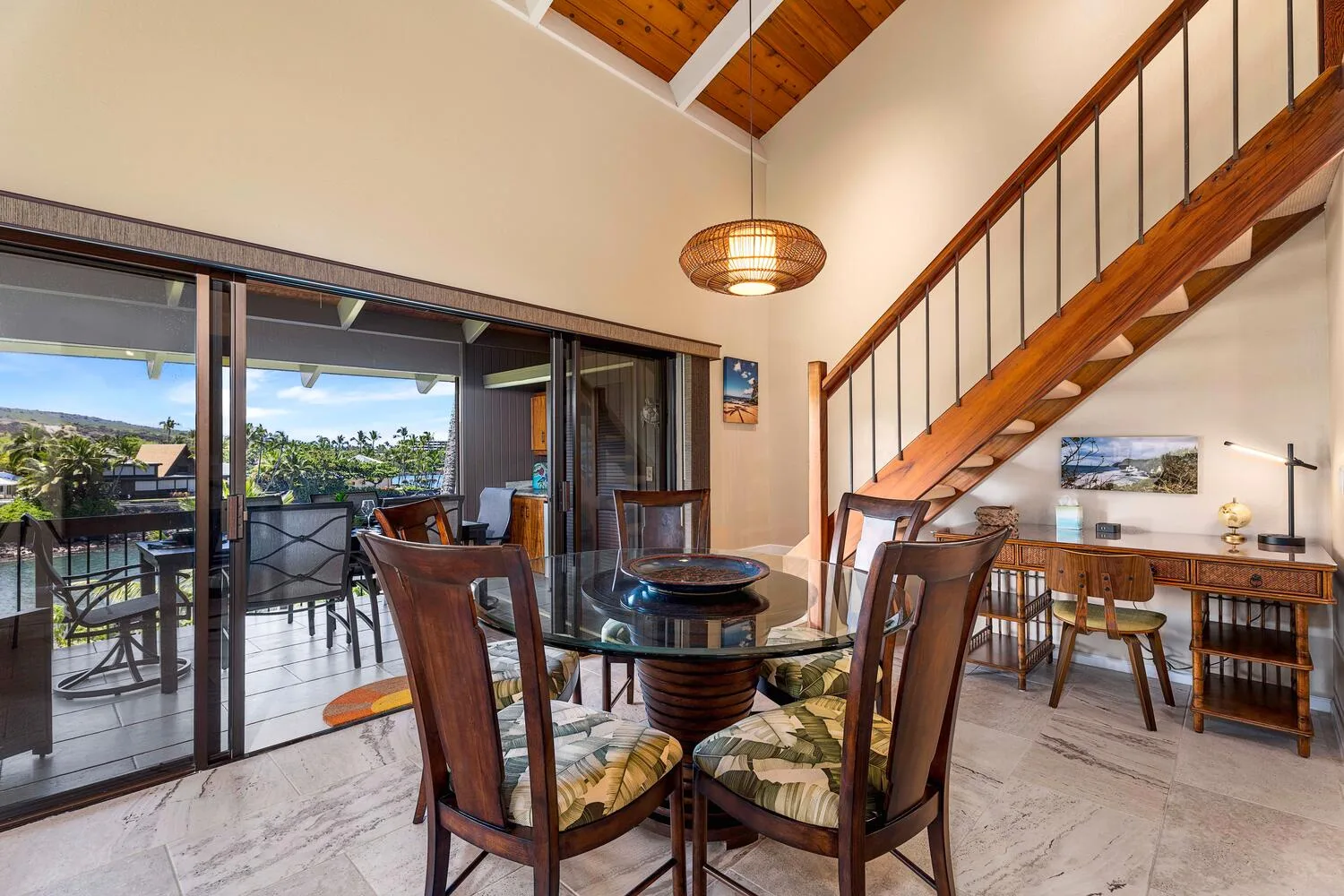 Comedor con una mesa de vidrio y una escalera de madera junto a grandes puertas corredizas.