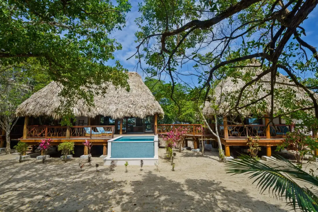 Thatched-roof pavilion buildings stand among trees beside a small pool.