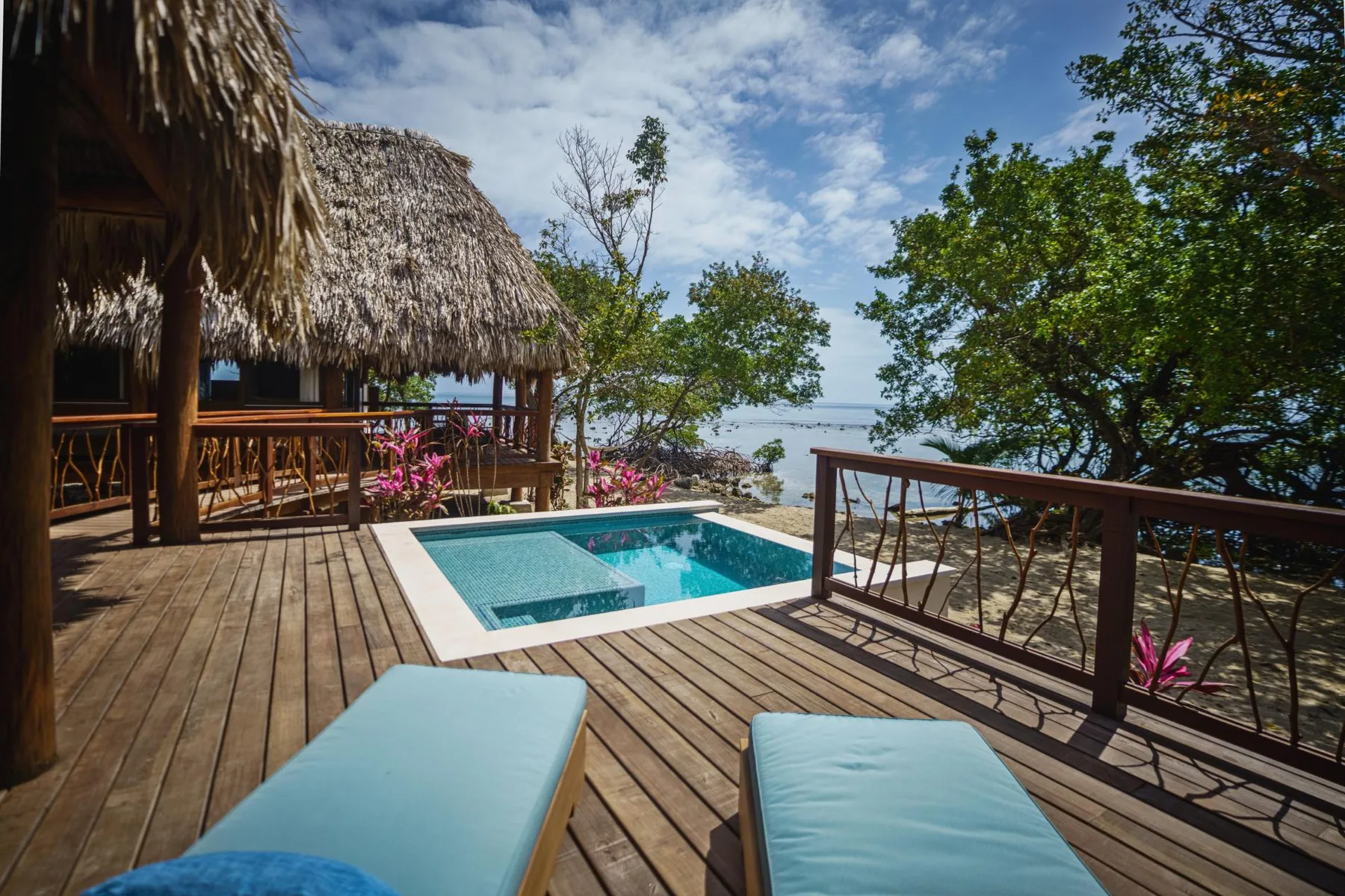 A wooden deck with a small pool overlooks the water beneath a partly cloudy sky.