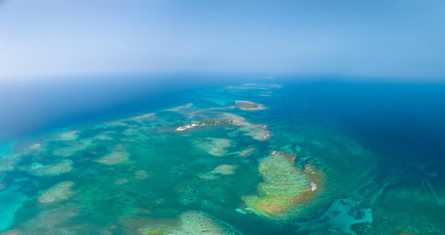 Aerial view of turquoise ocean surrounding scattered coral reefs.