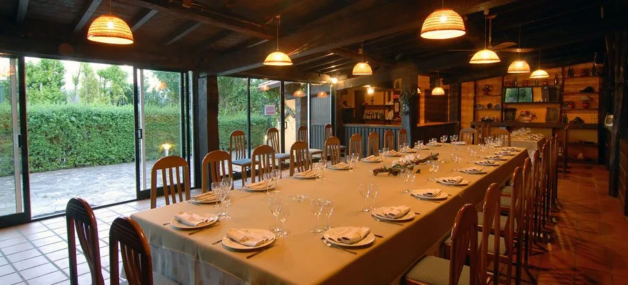 Salón de celebraciones preparado con una mesa larga y el jardín al fondo