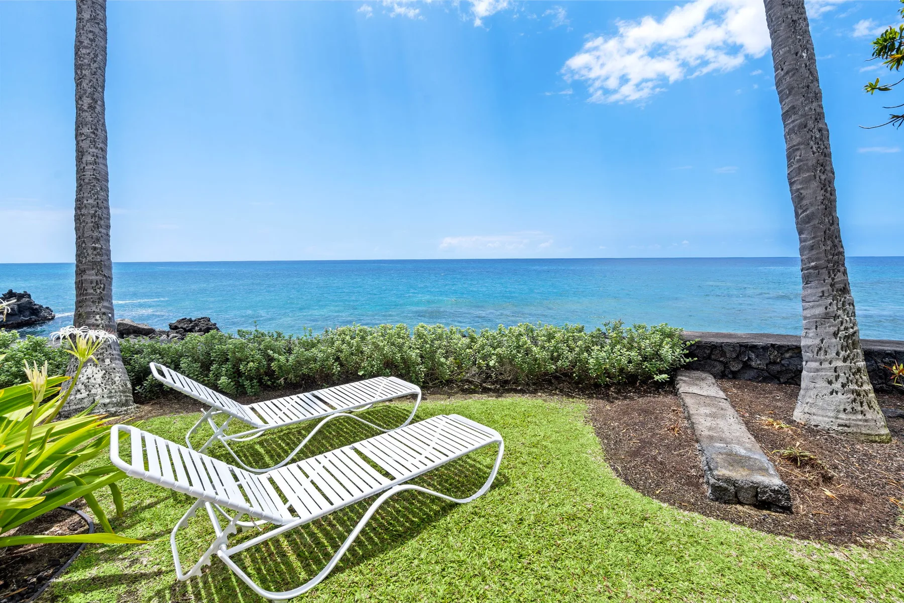 A seaside lawn with white lounge seating overlooks the ocean.