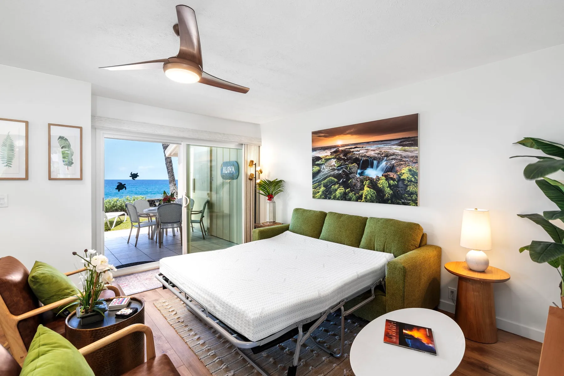 A bright bedroom with a bed, green seating, and an open view toward a balcony.