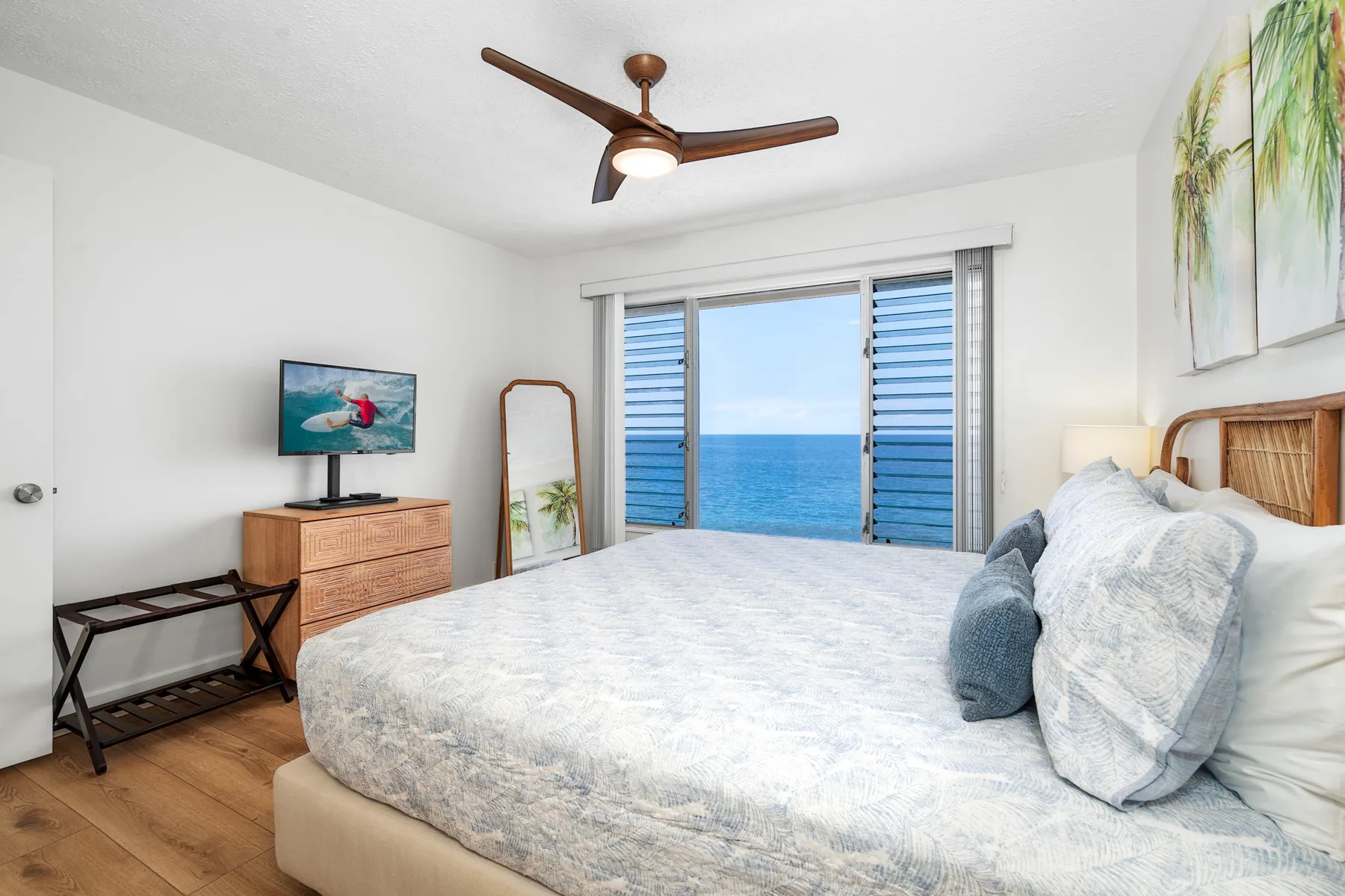 A bright bedroom with a large bed facing sliding glass doors overlooking the ocean.