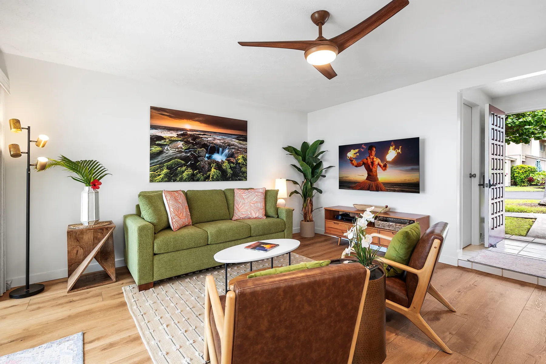 A living room with green seating, framed artwork, and an open doorway to a patio.