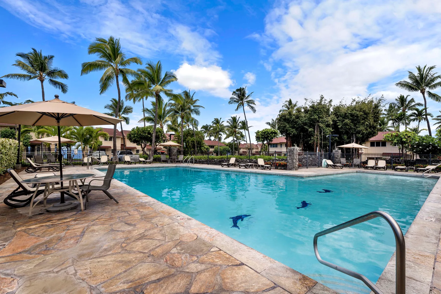 An outdoor swimming pool is surrounded by palm trees and lounge seating.