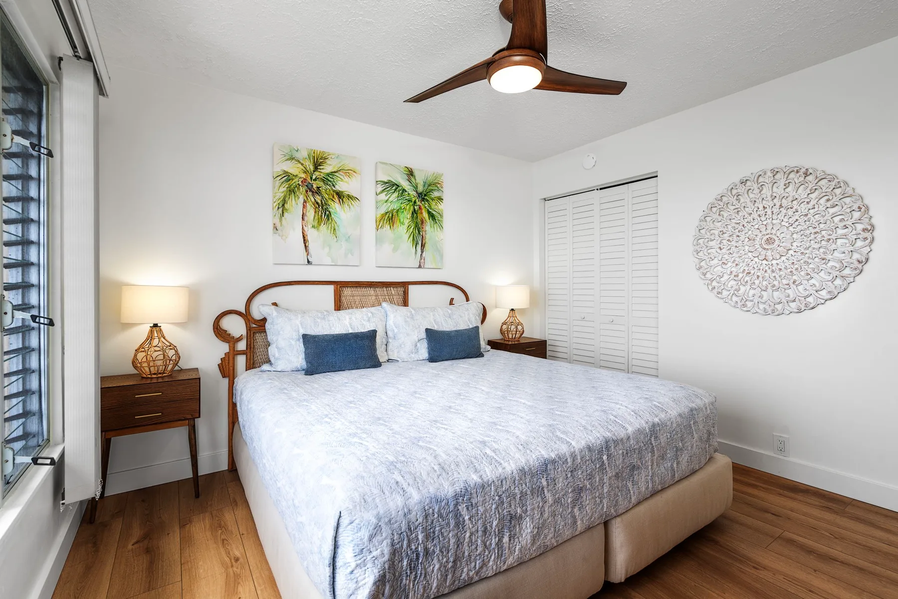 A bright bedroom with a neatly made bed and palm tree prints above the headboard.