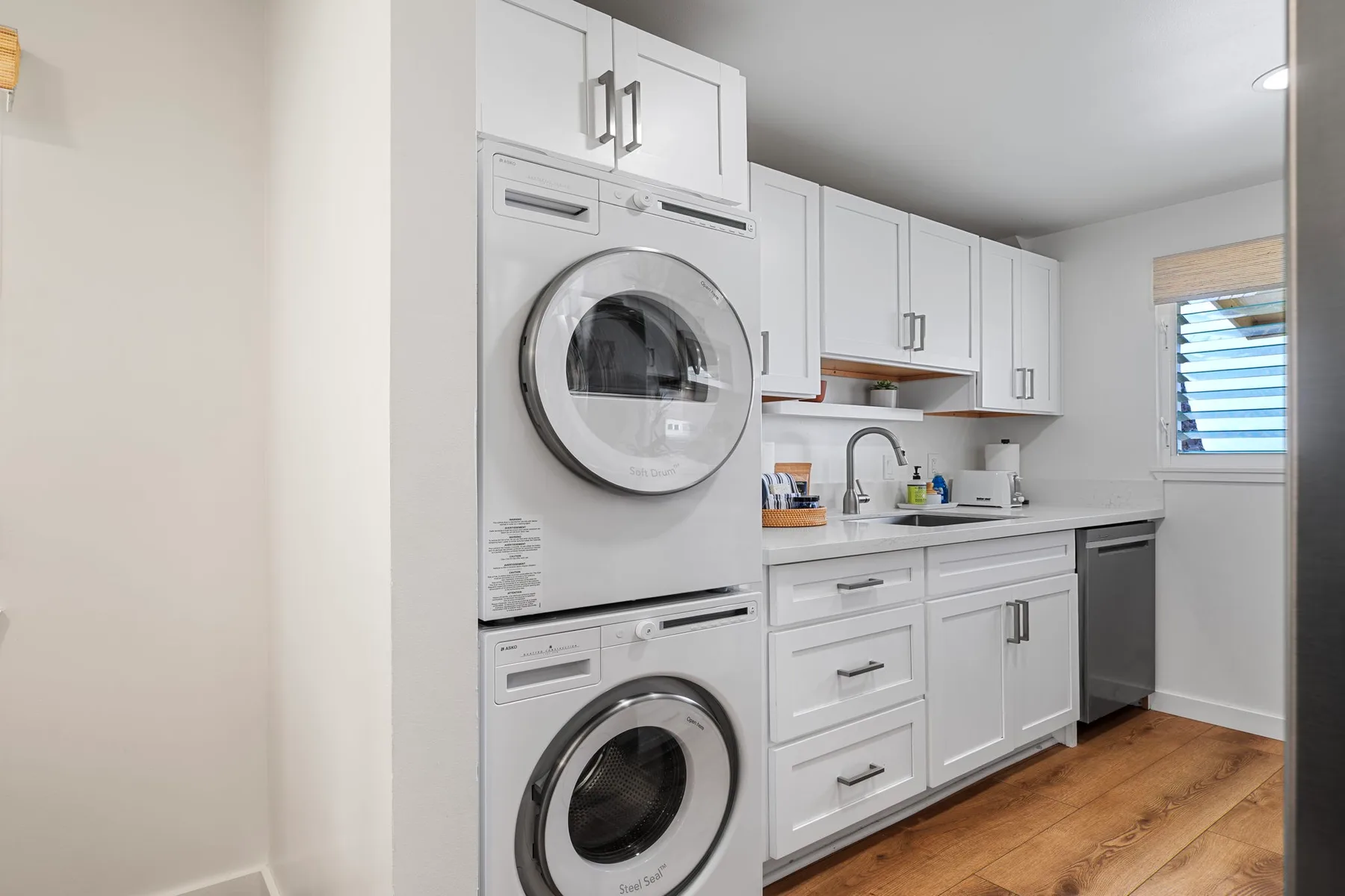 A laundry area with stacked appliances, white cabinets, and a sink.