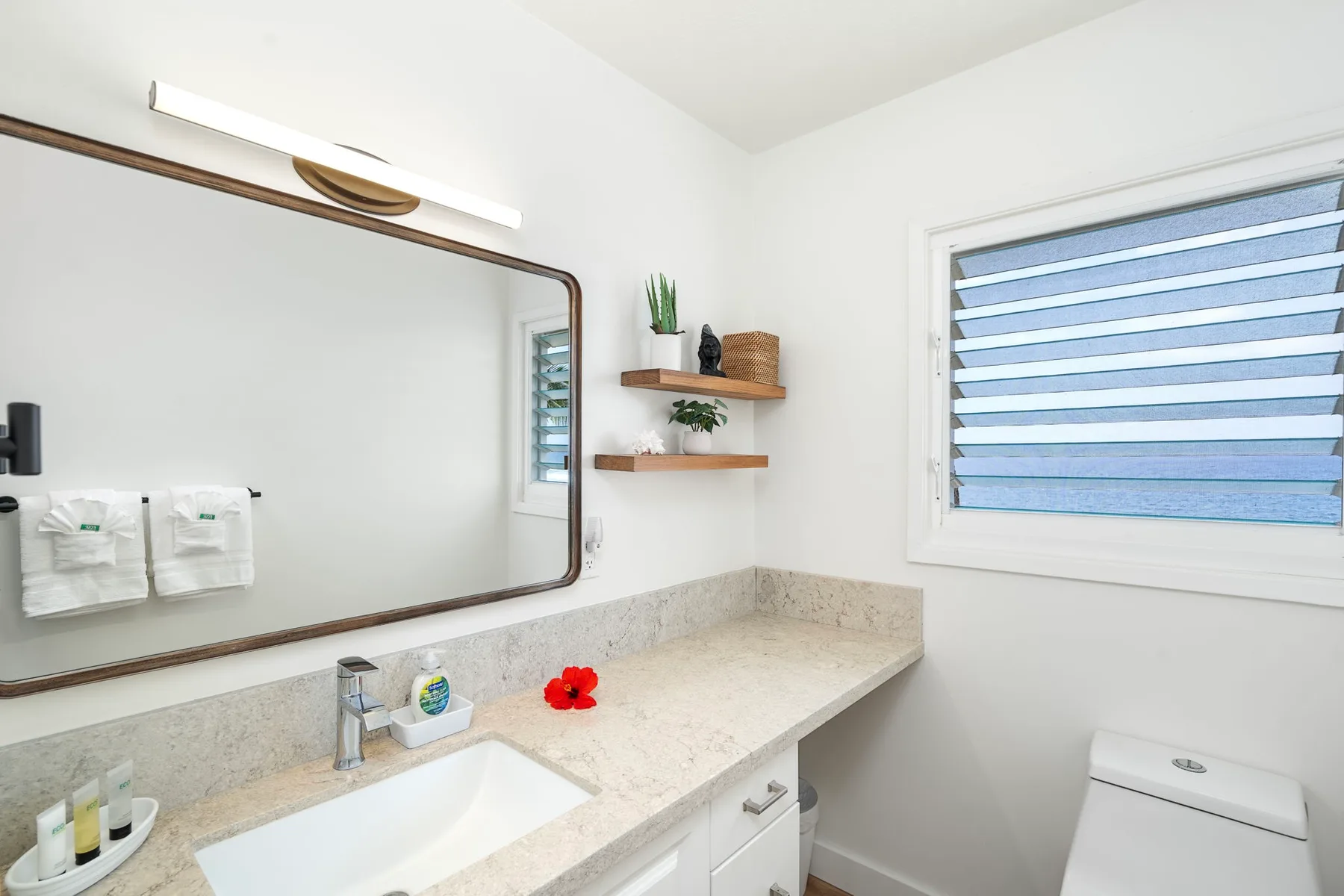 A bright bathroom with a sink, mirror, and window.