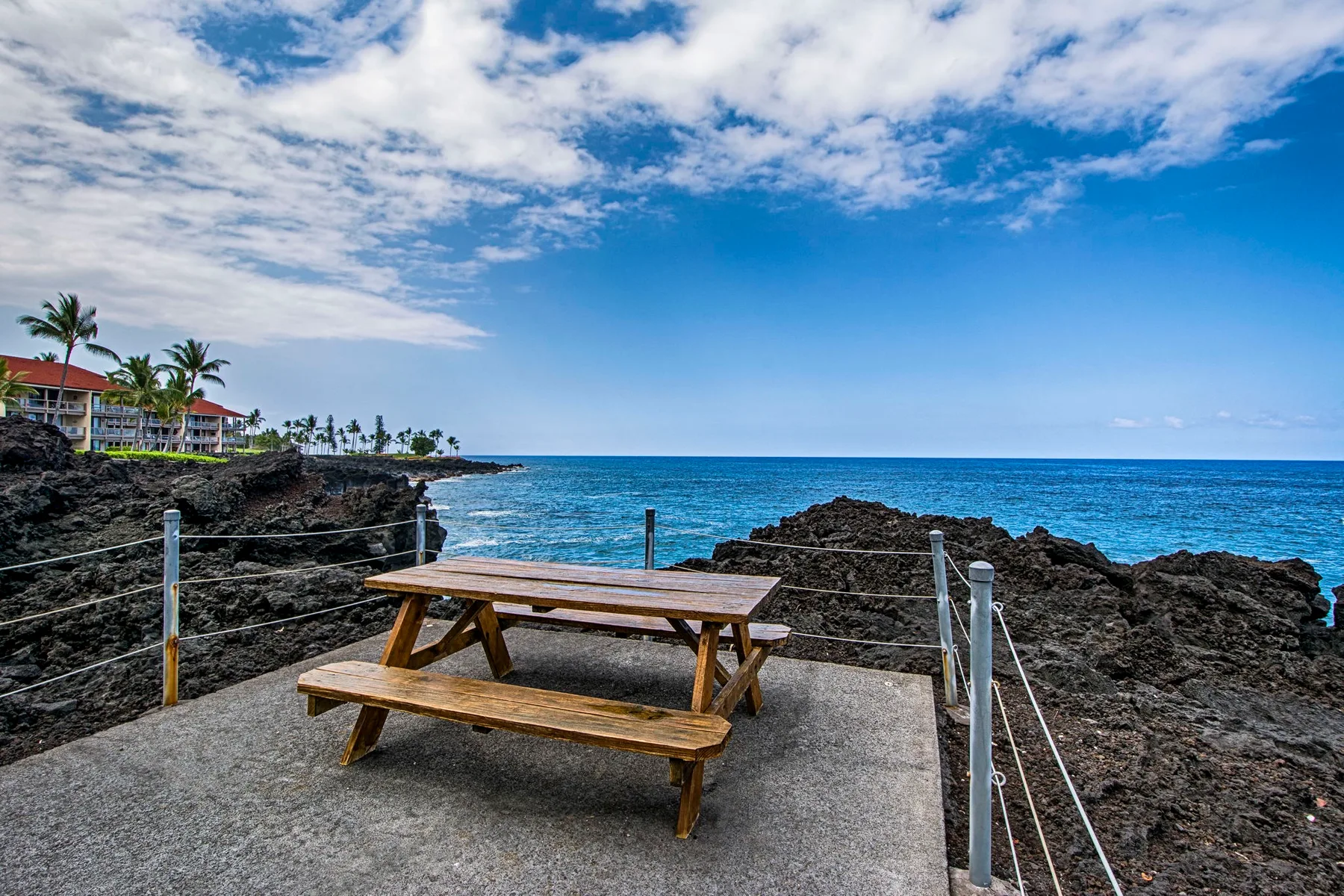 A picnic table sits on a rocky seaside terrace overlooking the ocean.