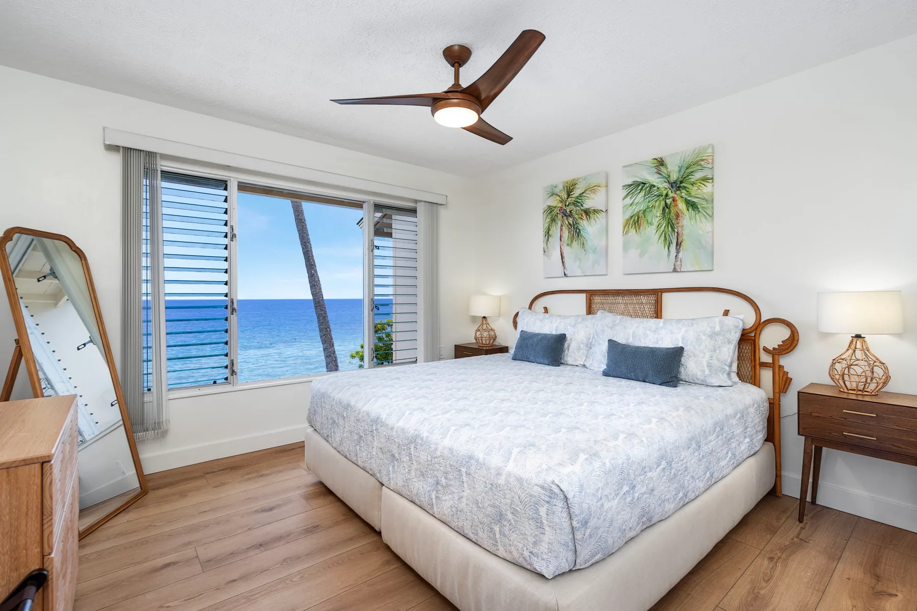 A bright bedroom with a large bed and sliding windows overlooking the ocean.