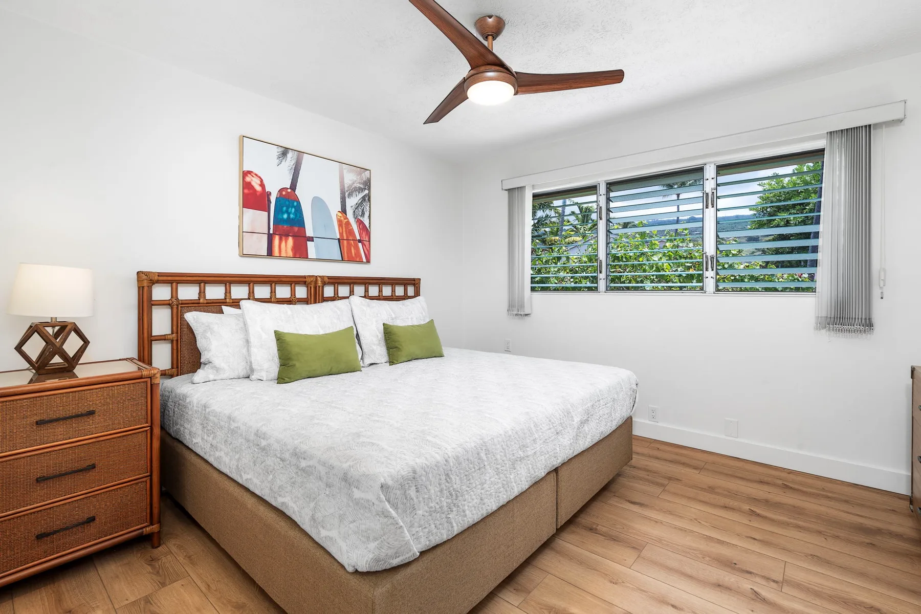 A bright bedroom has a bed beneath a window with horizontal blinds.