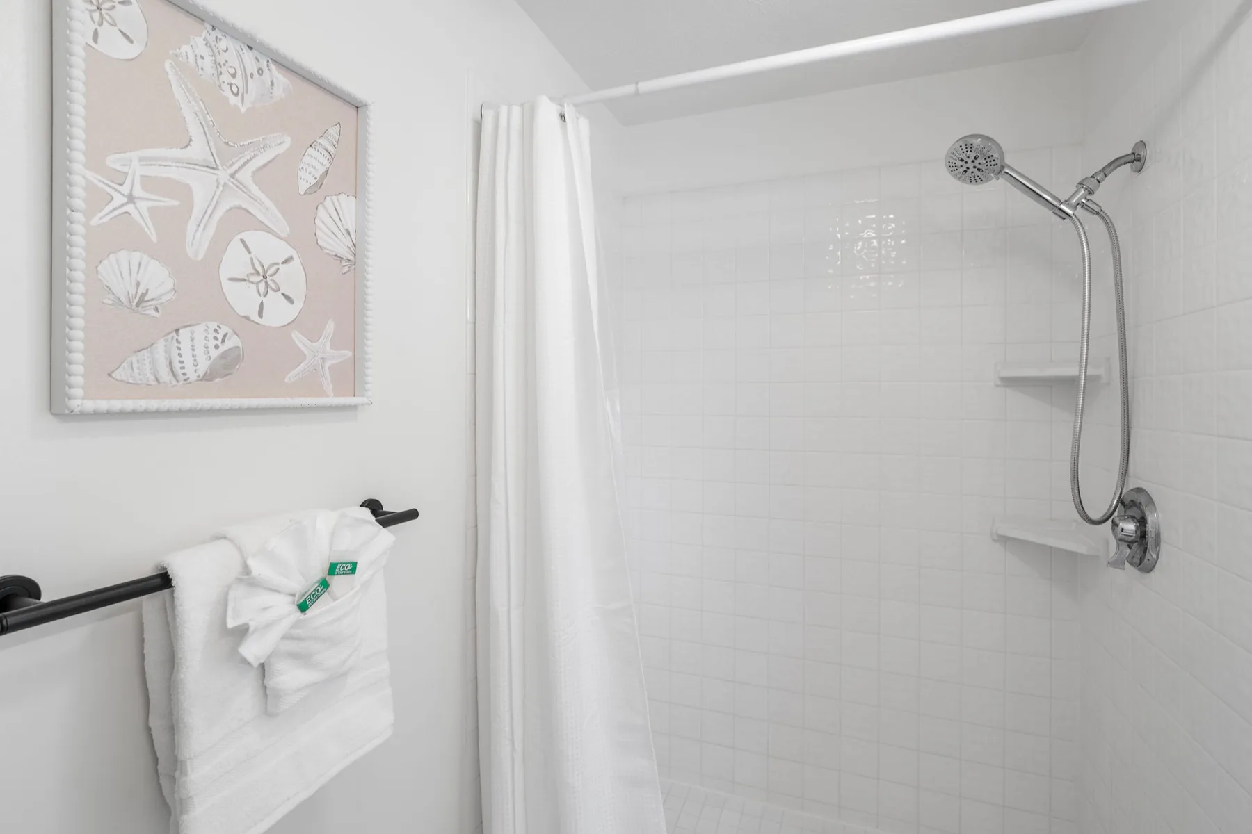 A tiled bathroom shower with a white curtain and towel hanging nearby.