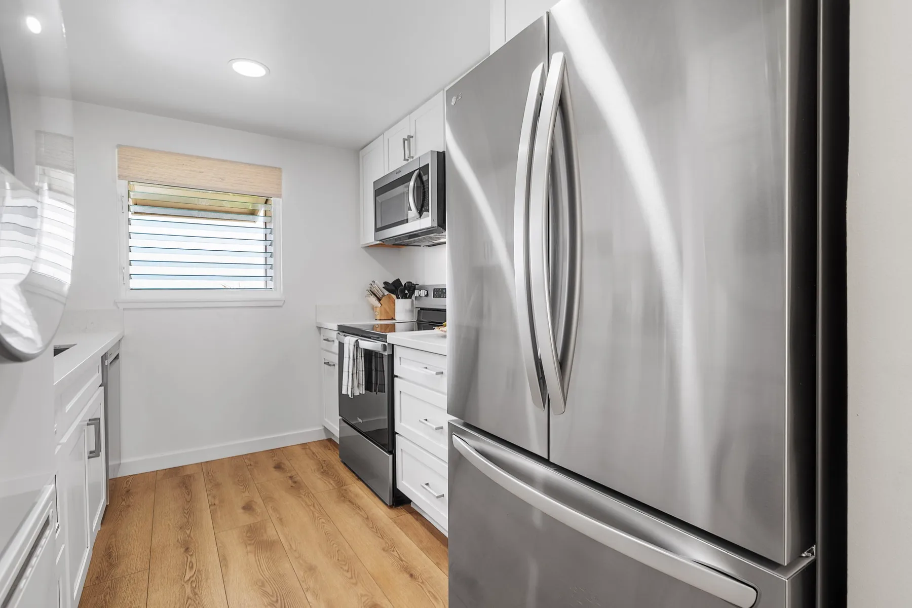 A bright kitchen with white cabinetry, wood flooring, and stainless steel appliances.