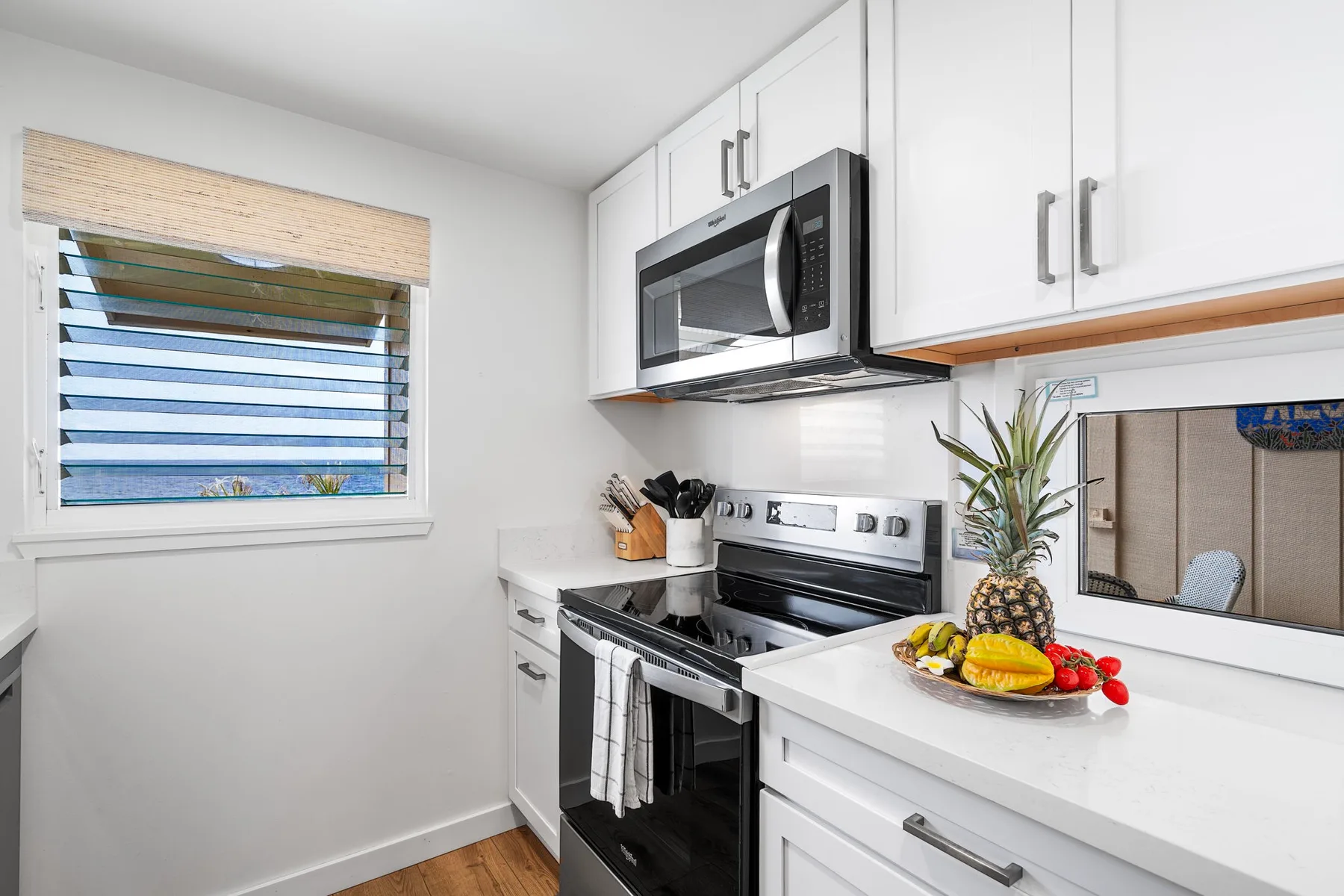 A bright kitchen with white cabinets, a stove, and fruit on the counter.