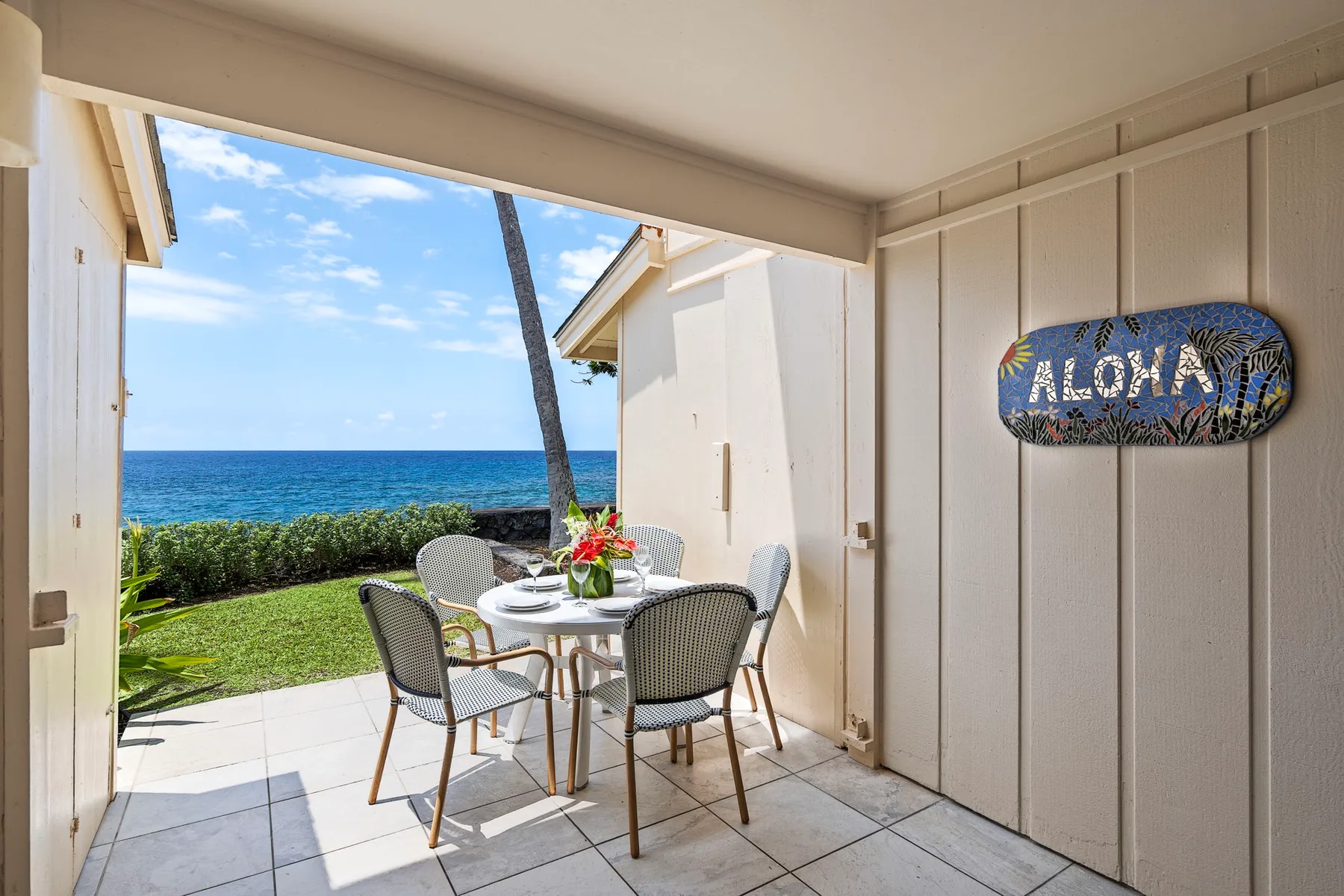 An outdoor patio dining area overlooks a garden and the ocean.
