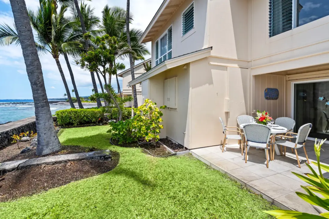 A coastal patio beside a light-colored building, with outdoor seating and a grassy lawn.