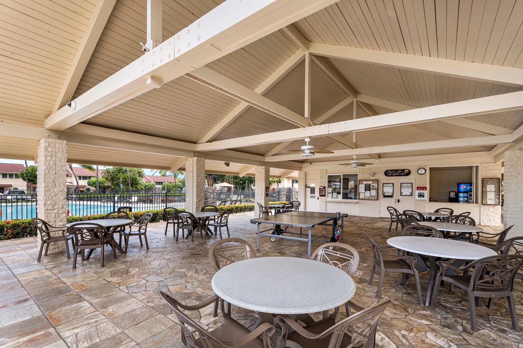 A covered outdoor seating area with tables and chairs beside a pool.