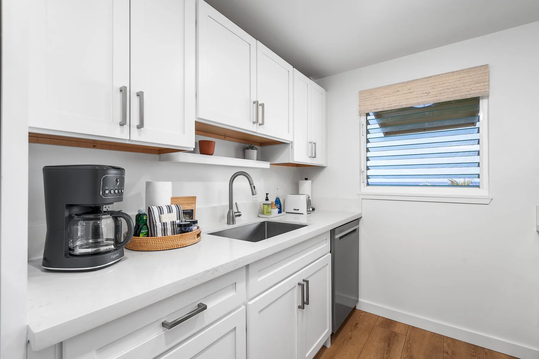 A bright kitchen with white cabinets, a sink, and a countertop coffee maker.