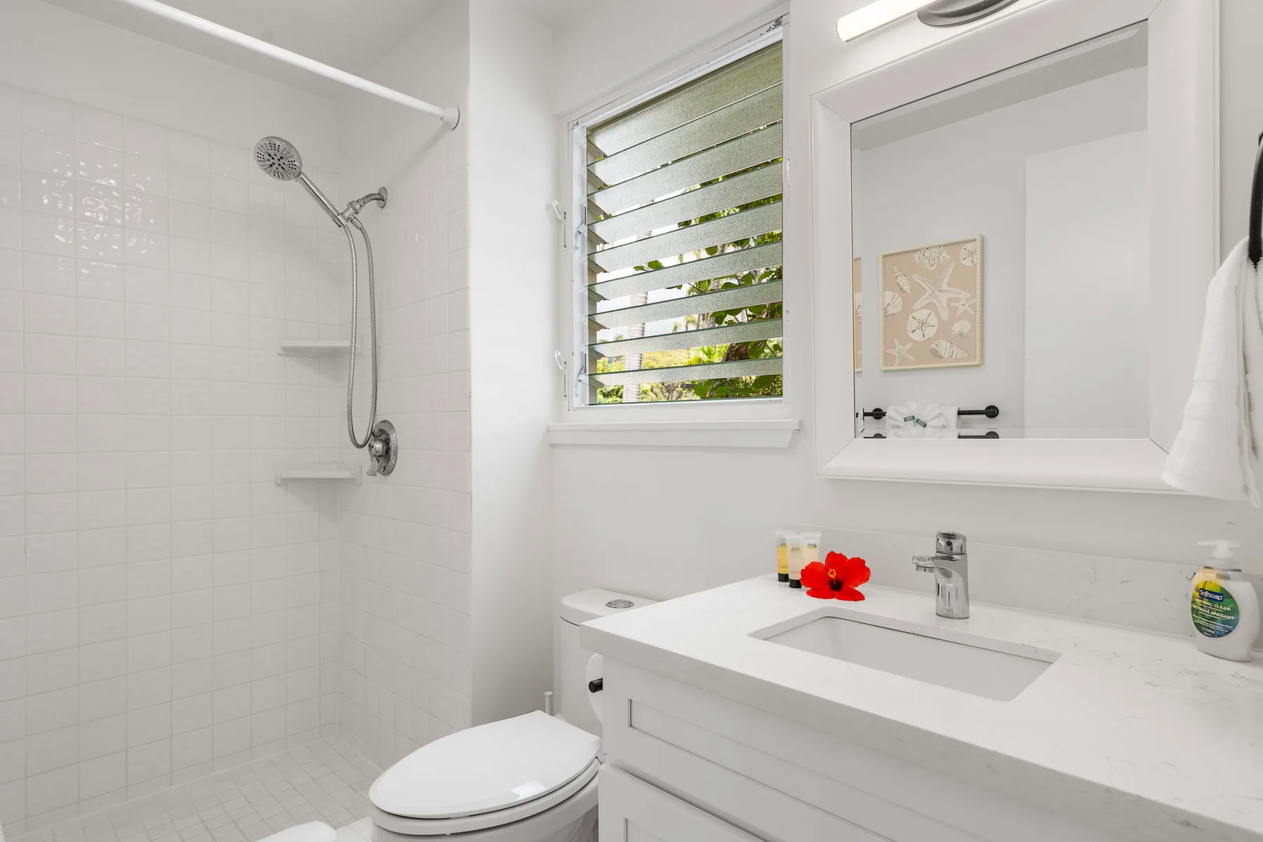 A bright bathroom with a shower, toilet, and white sink vanity.